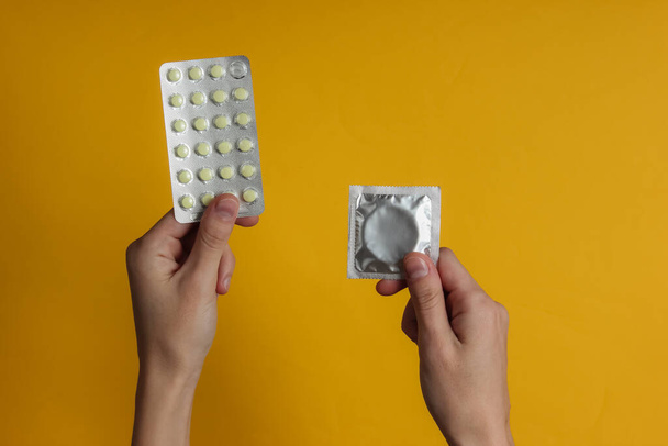 Mano sostiene condones en el embalaje, píldoras anticonceptivas sobre fondo amarillo. Vista superior. El concepto de preservación sexual - Foto, imagen