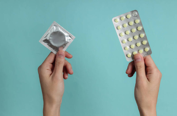Mano tiene preservativi nella confezione, pillole anticoncezionali su sfondo blu. Vista dall'alto. Il concetto di conservazione sessuale - Foto, immagini