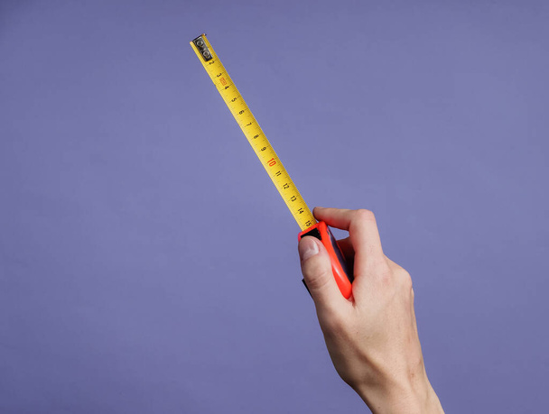 Female hands take measurements with industrial tape measure on purple background - Φωτογραφία, εικόνα