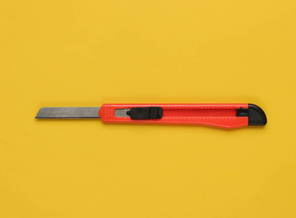 Канцелярский нож для резки бумаги на желтом фоне. Вид сверху - Фото, изображение