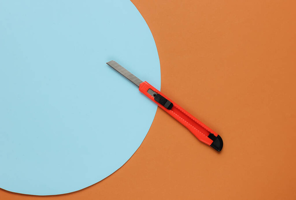 Schreibwarenmesser zum Schneiden von Papier auf farbigem Hintergrund. Ansicht von oben - Foto, Bild