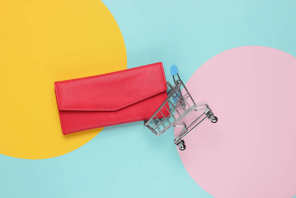 Concepto de compras minimalista. Carro de la compra, cartera de cuero rojo sobre fondo de papel de color - Foto, Imagen