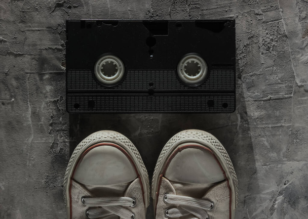 Stare trampki i kaseta wideo na szarym, betonowym tle. Widok z góry - Zdjęcie, obraz