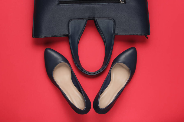 Klasyczne buty na wysokim obcasie, skórzana torba na czerwonym tle. Koncepcja mody minimalizmu. Widok z góry - Zdjęcie, obraz