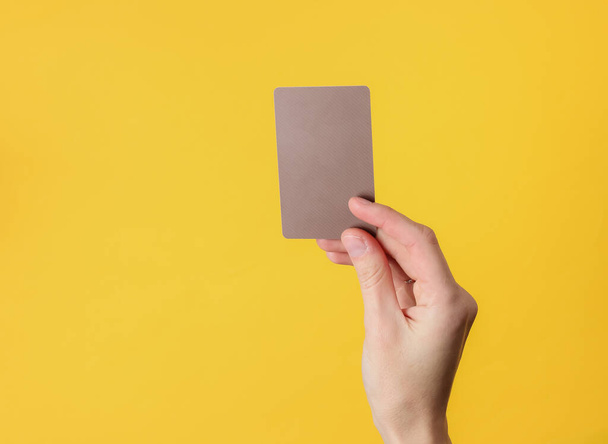La mano femenina sostiene una tarjeta de visita marrón en blanco sobre fondo amarillo - Foto, imagen