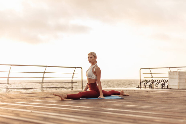 Здорова жінка практикує йогу на морській набережній. Спортивна жінка практикує шпагат на сході сонця
 - Фото, зображення