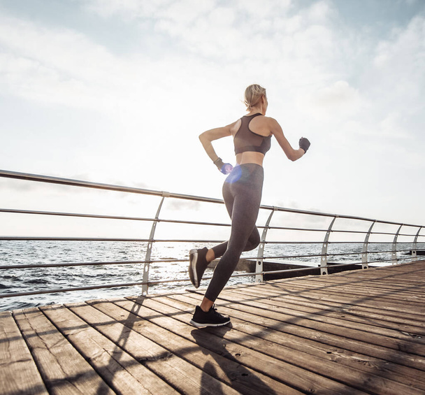 Morning run. Young athletic woman in sportswear runs on the beach at sunrise. Sprinter. Healthy lifestyle. Back view - Фото, зображення