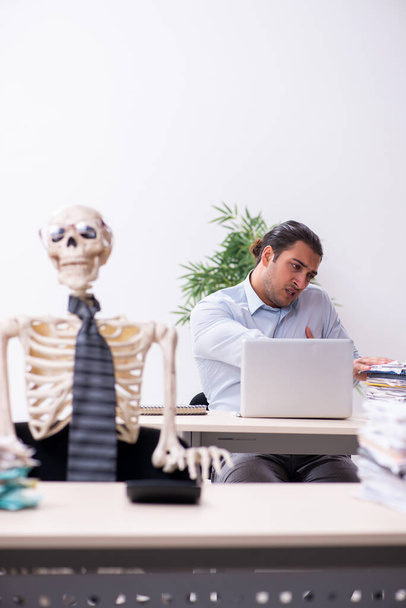 Молодой работник и скелет в офисе - Фото, изображение