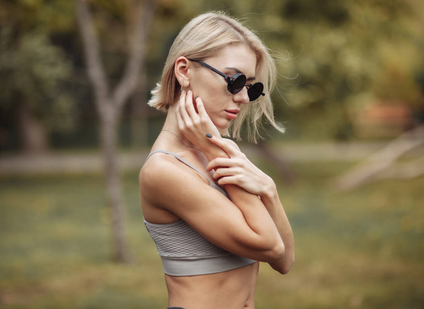 Portrait of fashionable blonde woman in stylish sunglasses in the park on bright sunny day - 写真・画像