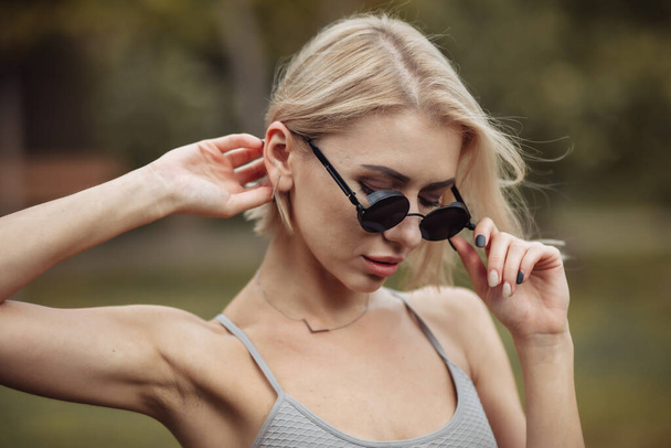 Porträt einer modischen blonden Frau mit stylischer Sonnenbrille im Park an einem sonnigen Tag - Foto, Bild