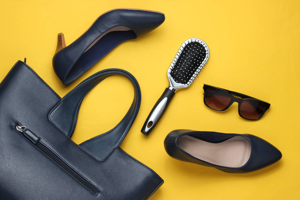 Accessoires pour femmes de style laïc plat sur fond jaune. Sac, chaussures à talons hauts en cuir, lunettes de soleil, peigne. Vue du dessus - Photo, image