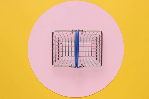 Mini shopping basket on yellow background with pink circle. Top view - Photo, Image