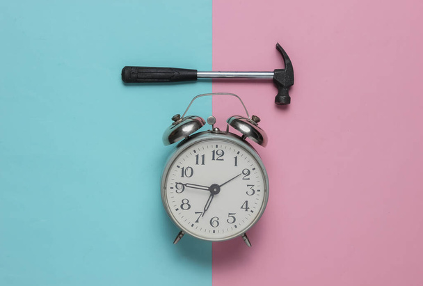 Reloj despertador con martillo sobre fondo azul rosado. Vista superior. Minimalismo - Foto, imagen