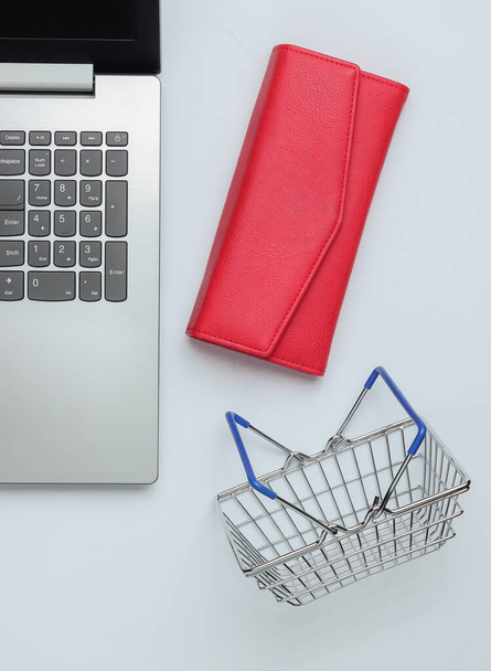 Online shopping concept. Laptop, wallet and mini shopping basket on white background. Top view - Photo, Image