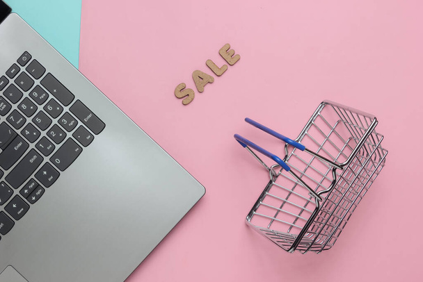 Концепция онлайн-покупок, распродажи. Ноутбук и мини корзина для покупок на розово-голубом пастельном фоне. Вид сверху - Фото, изображение