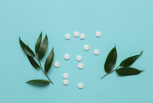 Herbal pills. White pills with green leaves on a blue pastel background. Minimalistic medicine still life - Fotografie, Obrázek