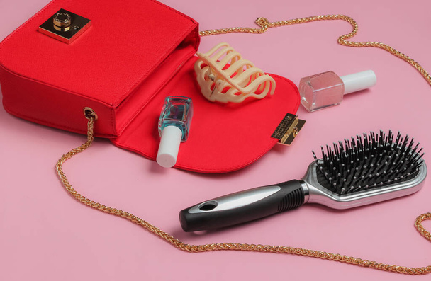 Τι είναι στην τσάντα των γυναικών. Κόκκινη δερμάτινη τσάντα με αξεσουάρ για γυναίκες, καλλυντικά προϊόντα σε ροζ φόντο. Μινιμαλιστική έννοια μόδας. Φωτογραφία στούντιο - Φωτογραφία, εικόνα