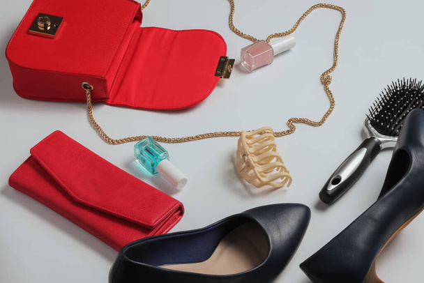Was ist in der Frauentasche? Rote Ledertasche mit Damenaccessoires, Kosmetikprodukten, Stöckelschuhen auf weißem Hintergrund. Minimalistisches Modekonzept. Studioaufnahme - Foto, Bild