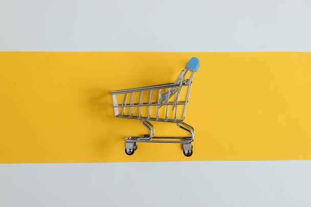Minimalistic shopping concept. Shopping trolley on white-yellow background. - Photo, Image
