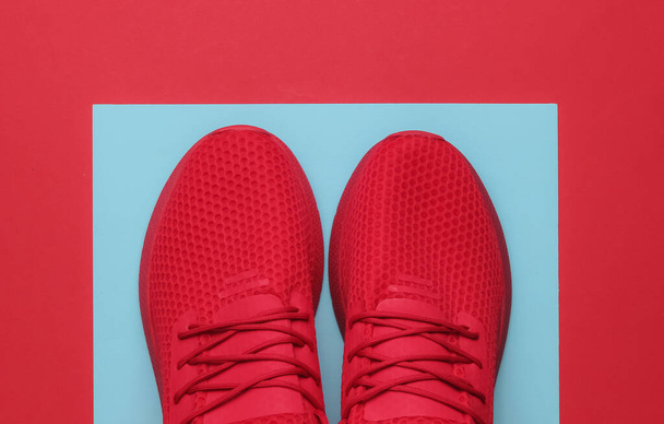 Czerwone sportowe buty do biegania na niebiesko-czerwonym papierowym tle. Widok z góry. - Zdjęcie, obraz