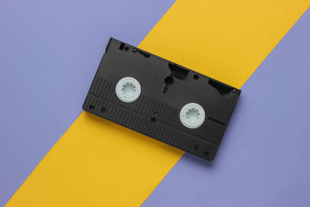 Retro kaseta wideo na żółto-fioletowym tle. Lata 80. Widok z góry - Zdjęcie, obraz