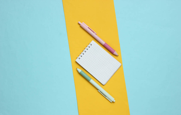 Ручки с ноутбуком крупным планом на синем желтом фоне. Тенденция пастельного цвета - Фото, изображение