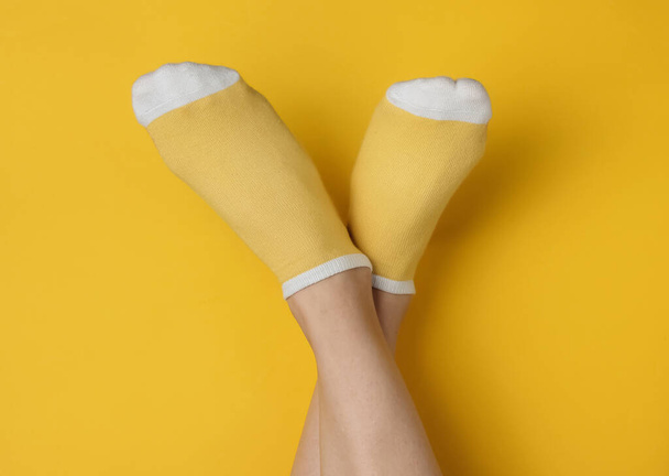 Женские ноги с жёлтыми носками на жёлтом фоне студии. Минималистическая концепция моды. Вид сверху - Фото, изображение
