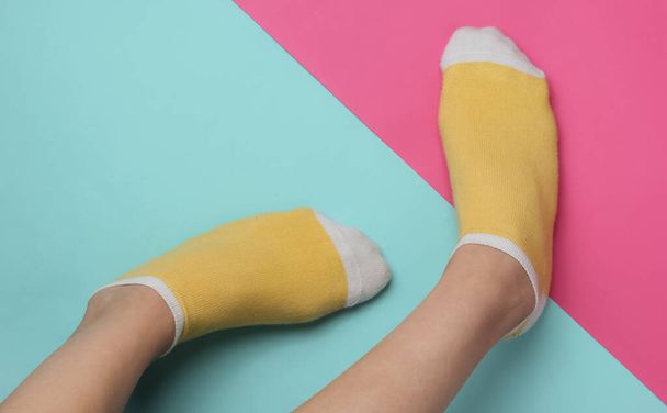 Female legs with yellow socks on pink blue studio background. Pastel color trend. Minimalistic fashion concept. Top view - Фото, изображение
