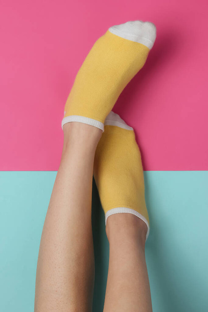 Vrouwelijke benen met gele sokken op roze blauwe studioachtergrond. Pastel kleur trend. Minimalistisch modeconcept. Bovenaanzicht - Foto, afbeelding