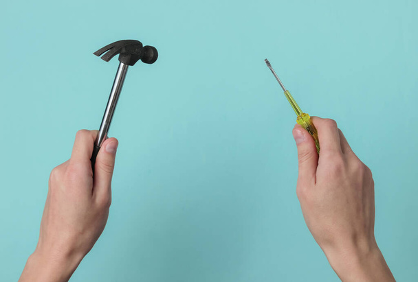 Repair concept. Female hand holds a screwdriver and a hammer on blue studio background. - Foto, afbeelding