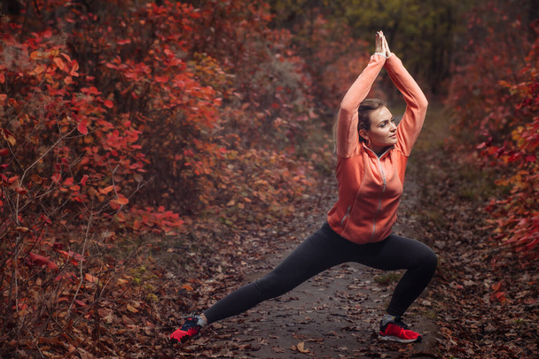 Joven mujer de corte delgado en ropa deportiva practicando ejercicio de yoga asana en el bosque otoñal con hojas enrojecidas - Foto, imagen