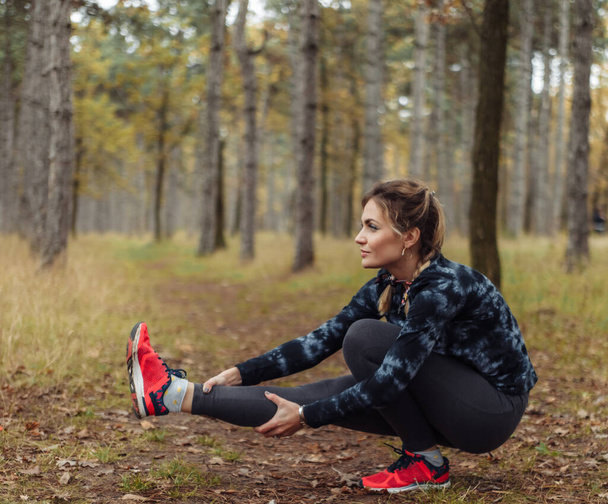 Young sport woman in sportswear doing squats on one leg in the autumn forest. Healthy lifestyle concept - Photo, image