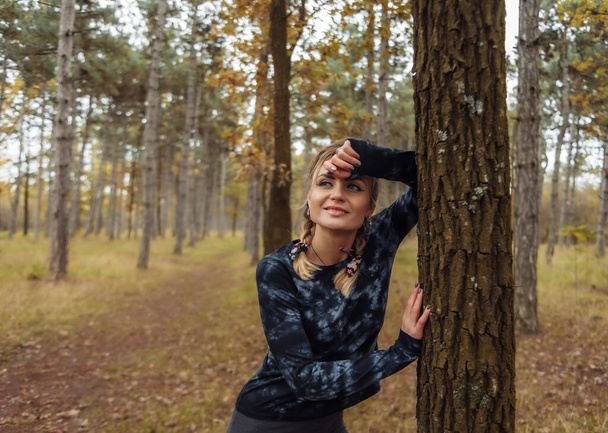 Young tired fit woman in sportswear leaned on a tree after an intense jog in the autumn forest. Healthy lifestyle concept. Outdoor workout - Photo, Image
