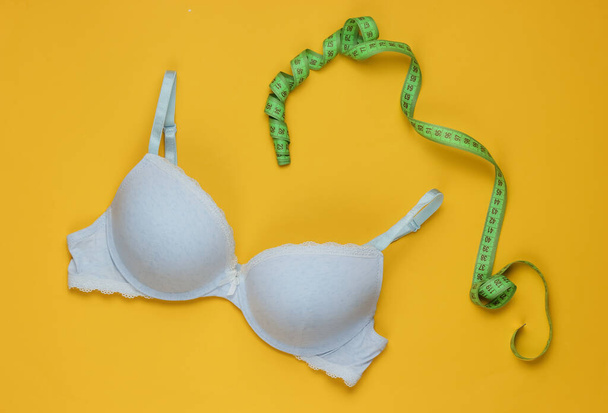 Soutien-gorge de sous-vêtements pour femmes et ruban à mesurer sur fond jaune. Concept de perte mammaire, mesure buste. Vue du dessus - Photo, image