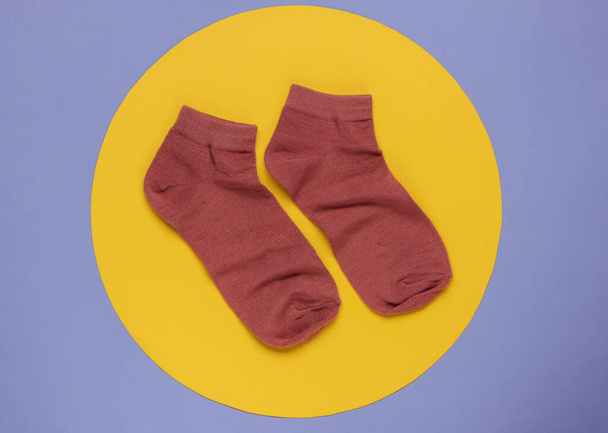 Red socks on a purple background with a yellow circle in the middle. Minimalistic fashion still life. Top view - Photo, Image