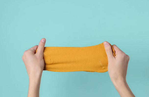 Female hands holding orange socks on a blue background. Top view - Photo, Image
