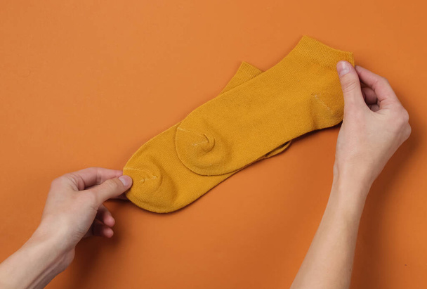 Női kezek narancssárga zoknival a barna háttéren. Felülnézet - Fotó, kép