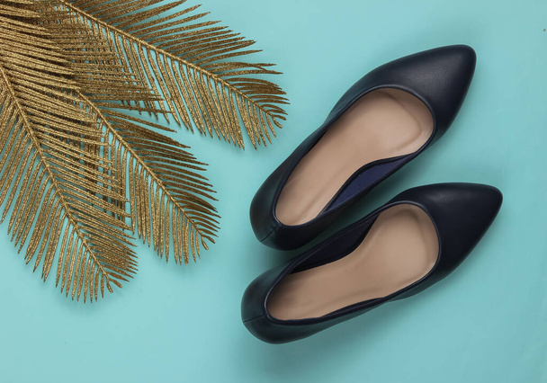 Mode minimaliste nature morte. Chaussures à talons classiques avec des feuilles de palmier doré sur fond bleu pastel. Prise de vue. Vue du dessus - Photo, image