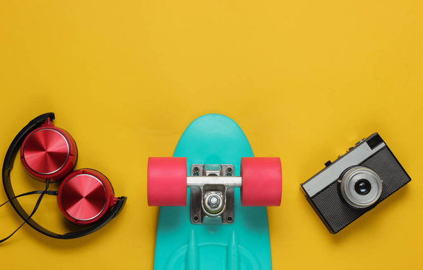Cruiser board, headphones, film camera on yellow background. Summer fun. Retro style. 80s. Top view - Zdjęcie, obraz
