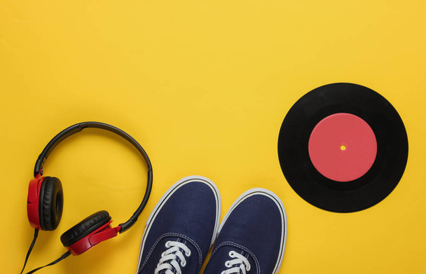 Stylische Kopfhörer, Old-School-Turnschuhe, Schallplatte auf gelbem Hintergrund. Retro-Stil. 80er Jahre. Popkultur. Ansicht von oben - Foto, Bild