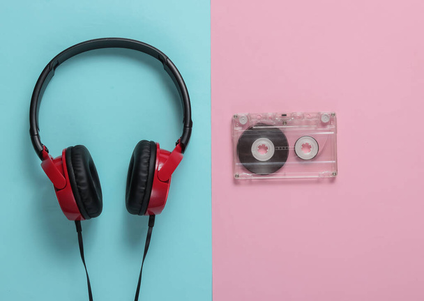 Kabelová sluchátka s audio kazetou na modrém růžovém pastelovém pozadí. Retro styl, DJ. Top view, minimalistický hudební koncept. - Fotografie, Obrázek