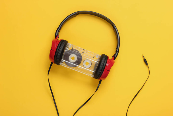 Wired headphones with audio cassette on yellow background. Retro style, DJ. Top view, minimalistic music concept. - Photo, Image