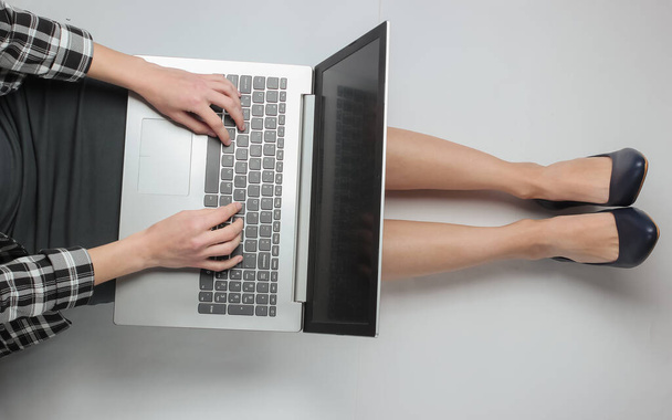 Деловая женщина в формальной одежде наслаждается ноутбуком, сидя на белом фоне. Удаленная, онлайн работа, офисный работник. Вид сверху - Фото, изображение