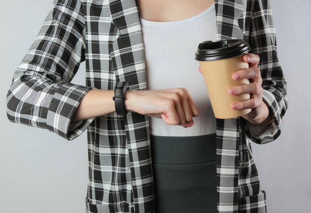 A business woman in formal clothes looks at her watch and holds a cup of coffee on a white background. Office worker, crop photo - Foto, afbeelding