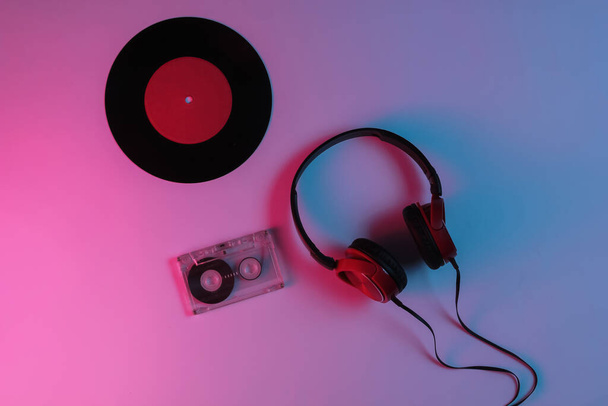 有線ヘッドフォン、ビニールレコード、ネオン青赤グラデーションライト付きオーディオカセット。レトロな波、 80年代ポップカルチャー。トップ表示 - 写真・画像