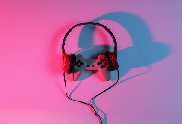 Kabelgebundene Kopfhörer mit Gamepad. Neon blau-rotes Gradientenlicht. Retro-Welle, Popkultur der 80er Jahre. Ansicht von oben - Foto, Bild