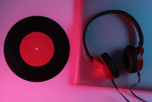 Lptop con auriculares y un disco de vinilo. Luz de gradiente azul-rojo neón. Retro wave, cultura pop, equipo de DJ. Vista superior - Foto, Imagen