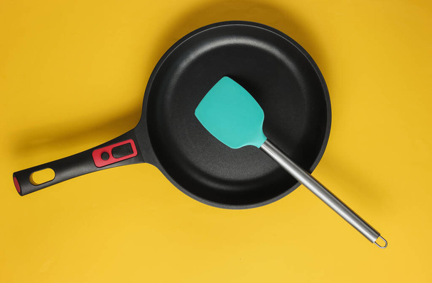 Non-stick pan with cooking spatula on yellow background. Cooking minimalism concept. Studio shot. Top view - Фото, зображення