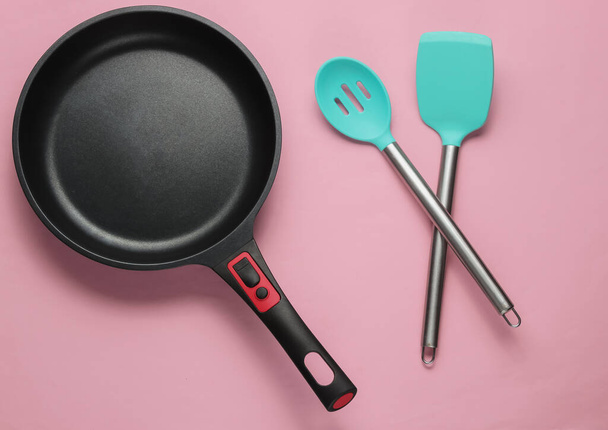 Non-stick pan met kookspatel op roze pastelachtergrond. Koken minimalisme concept. Een studio opname. Bovenaanzicht - Foto, afbeelding