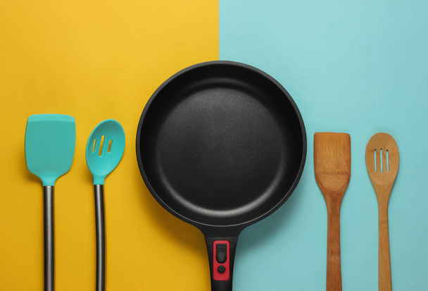 Non-stick pan with cooking spatula on blue yellow background. Cooking minimalism concept. Studio shot. Top view - Photo, Image